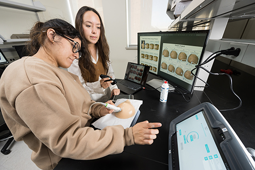 Two graduate students using an ultrasound on a model of a breast.
