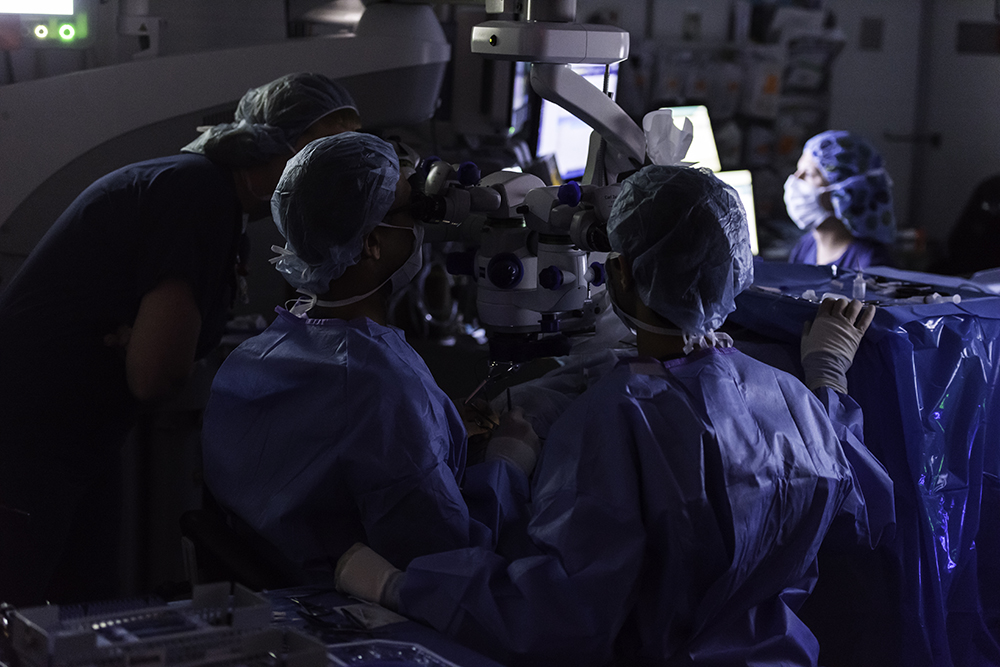 A group of people in a darkened surgery room wearing scrubs.