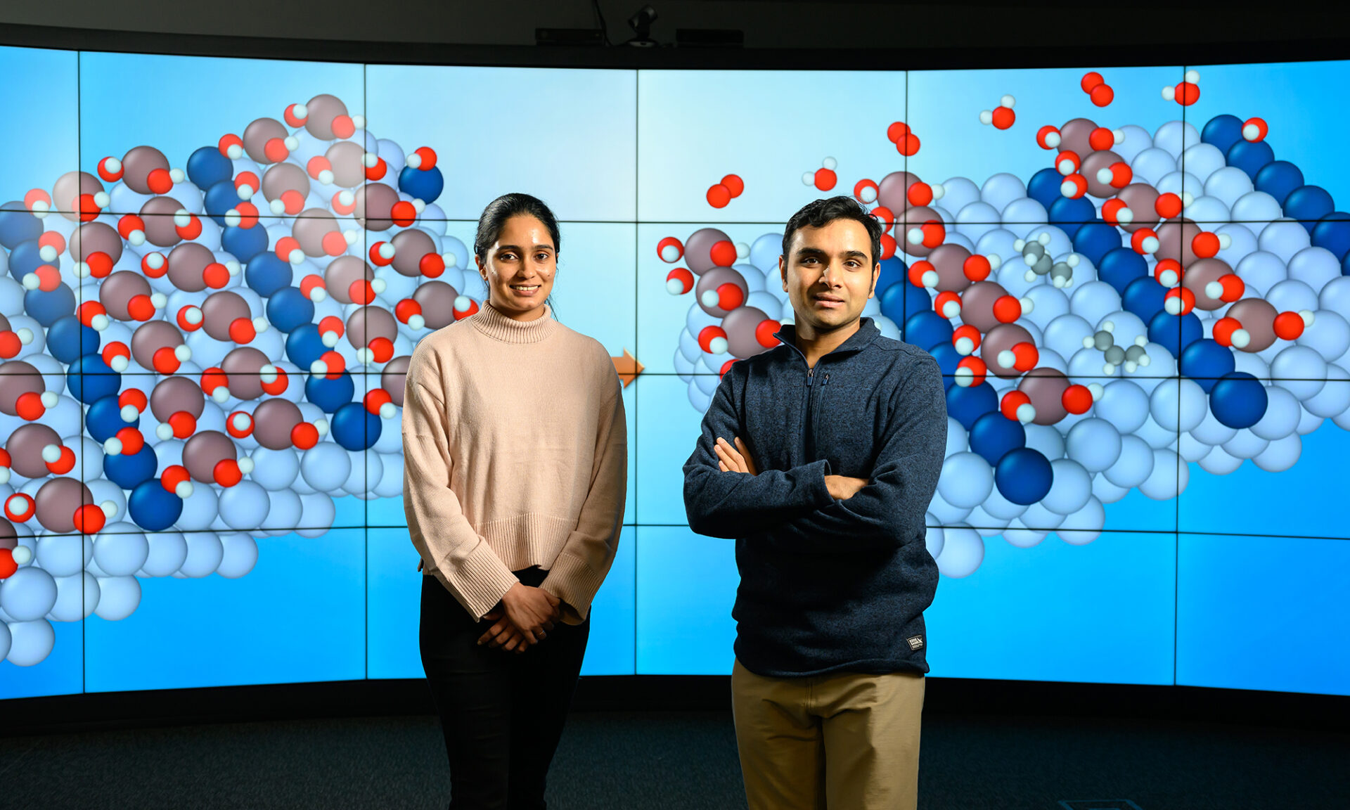 Siddharth Deshpande and Snehitha Srirangam standing in front of a large screen showing molecule simulations.