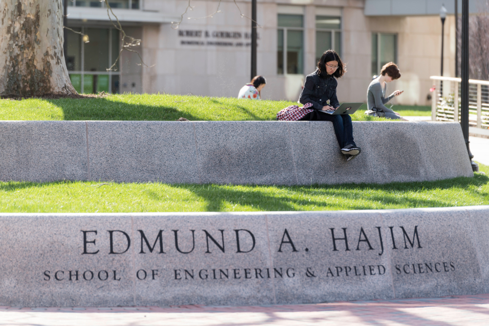 Students seen sitting on a low stone wall.