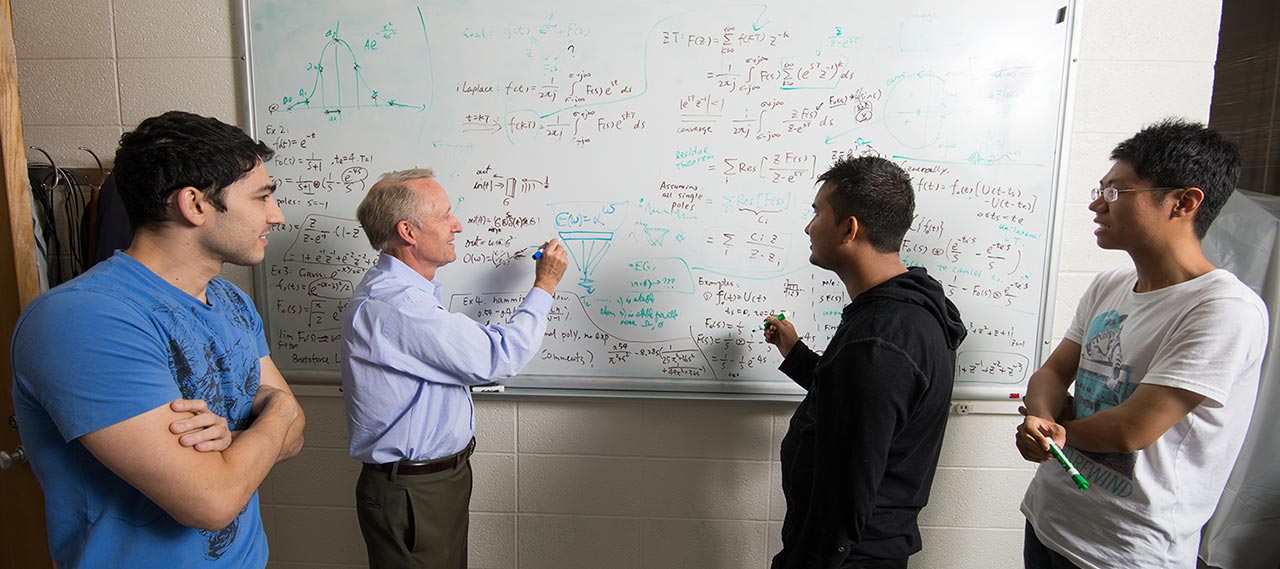 A professor at a white board with graduate students.