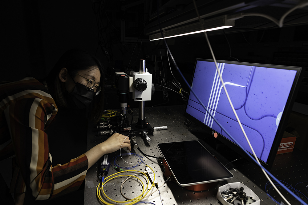 A student uses a microscope to check an integrated photonic chip.