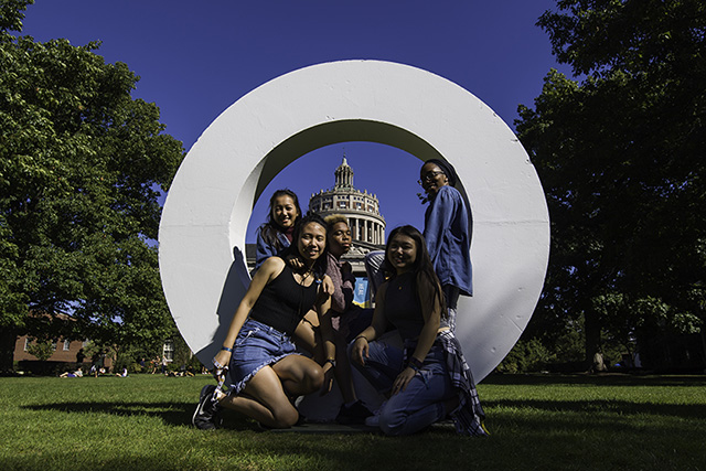 A smiling group of diverse students gathered in a large letter O on the Eastman Quad.