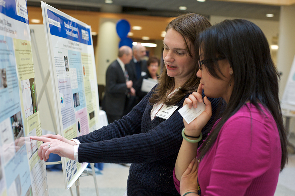 A student displaying a poster at a networking event.