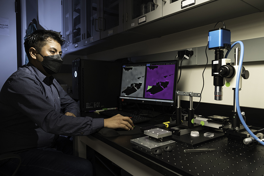 A person seen using a computer to view an image under a microscope.