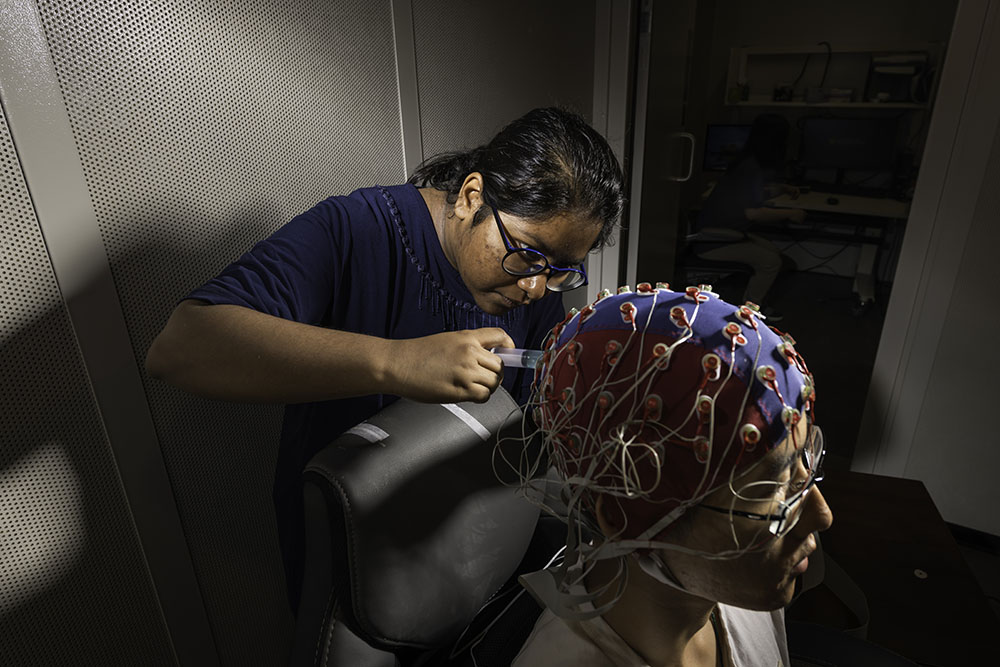 A biomedical engineering student adjusts an electroencephalography cap on fellow lab member.