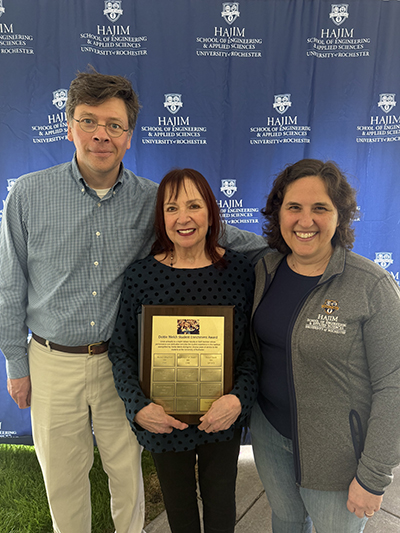 Three people smiling for the camera with the center person holding an award.