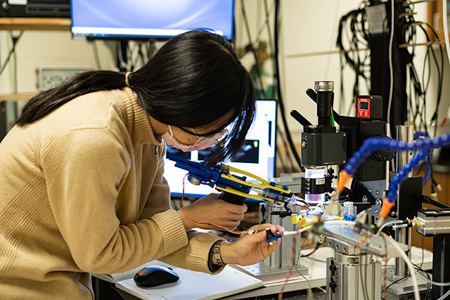 PhD student uses a custom-built device to exchange fluids in the microfluidic chamber.