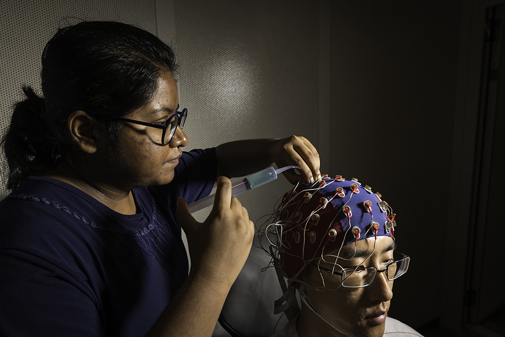 Senior biomedical engineering student adjusts an electroencephalography cap on a fellow lab member.