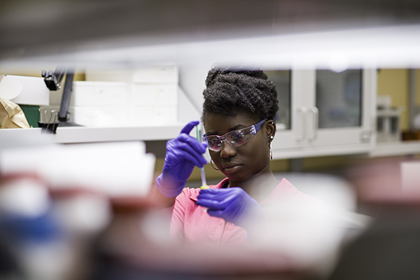 A lab assistant is pictured with a pipette.