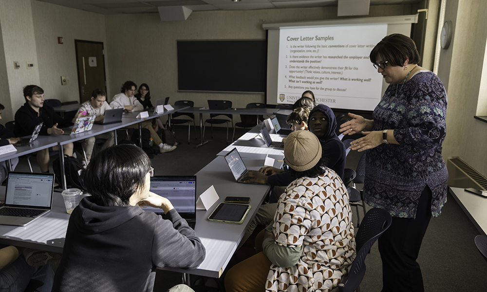 A classroom with a screen projector and an instructor helping students.