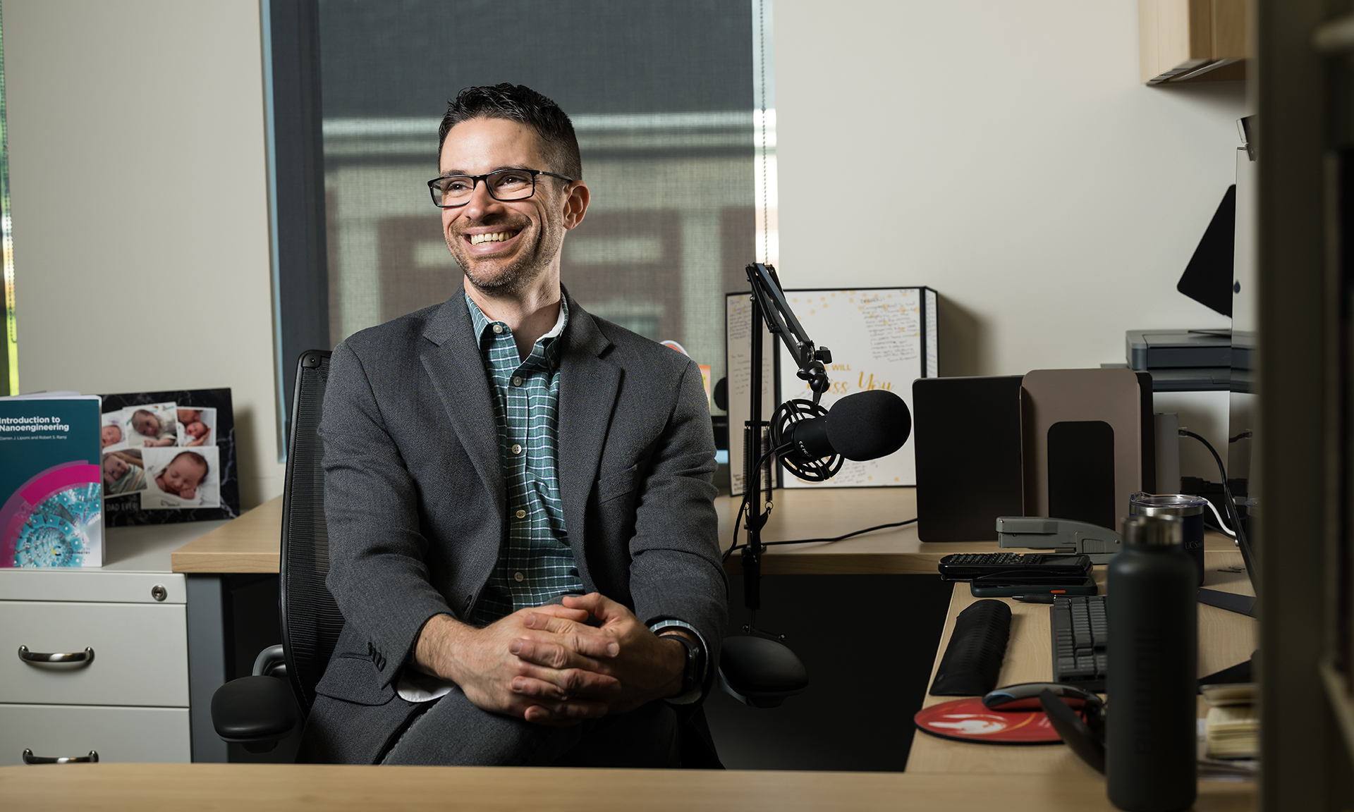 Darren Lipomi, smiling at sitting at his desk surrounded by video and audio recording equipment.