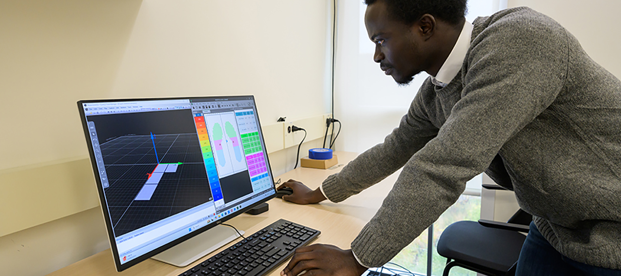A student leaning over a desk with a computer checking data on the screen.