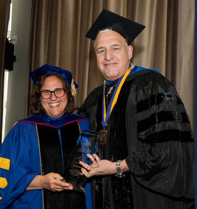 Eby Friedman received award from Wendi Heinzelman wearing cap and gowns