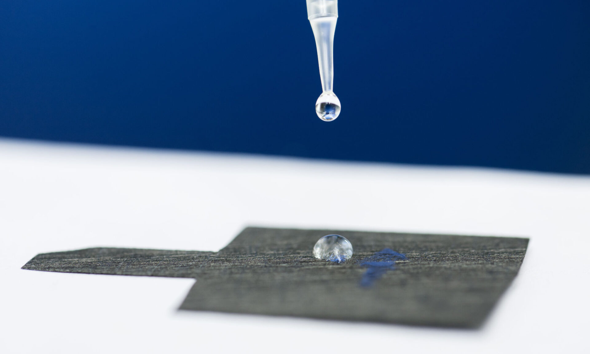 Pipette releasing a water droplet atop carbon paper to illustrate the remediation of pfas forever chemicals.