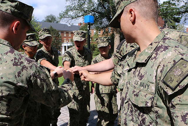 A group of recruits putting their hands together for a cheer.