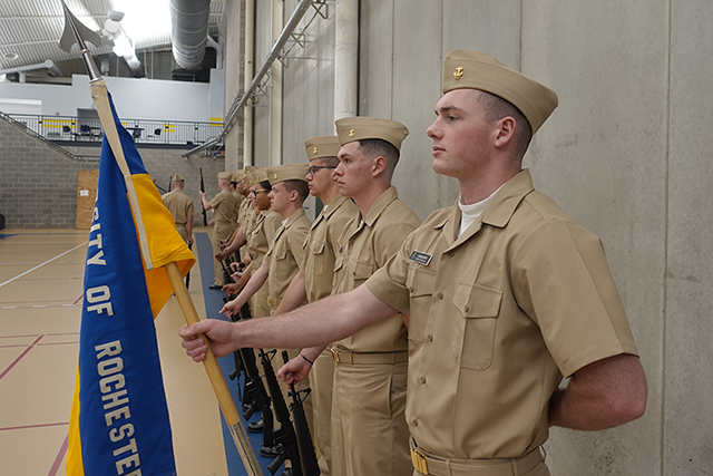 A midshipman holding the UR NROTC flag and standing at attention.