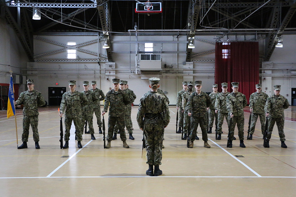 Midshipman lining up in formation in a large room.