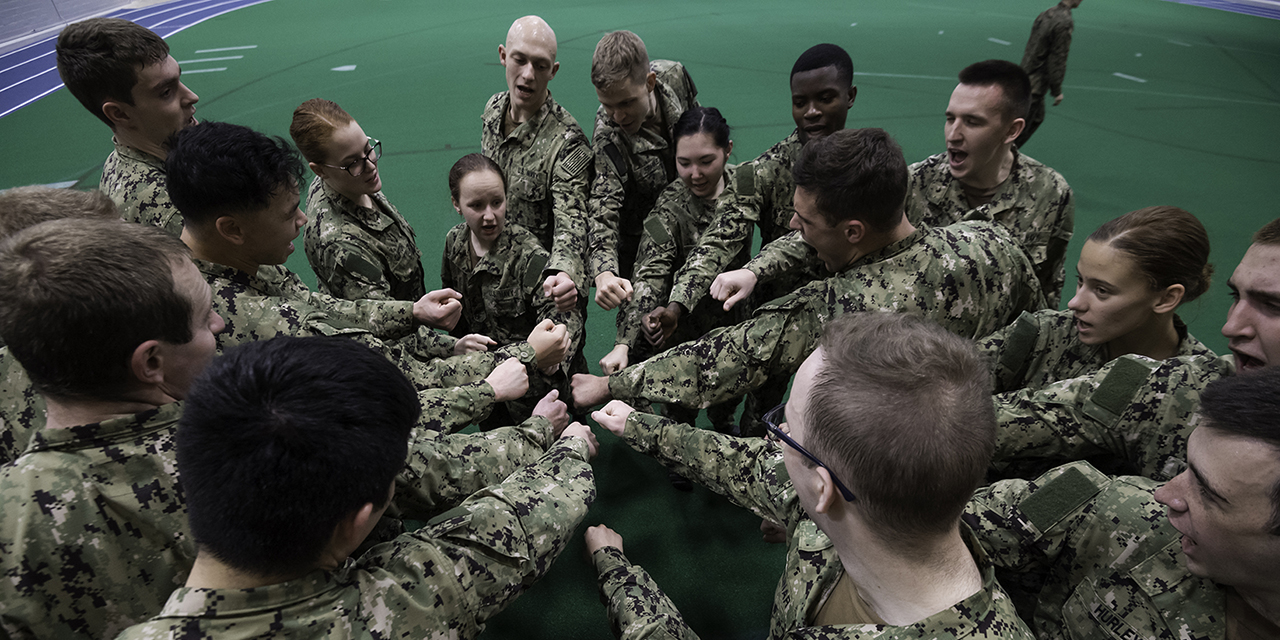 A group of midshipman seen from above putting their hands together for a cheer.
