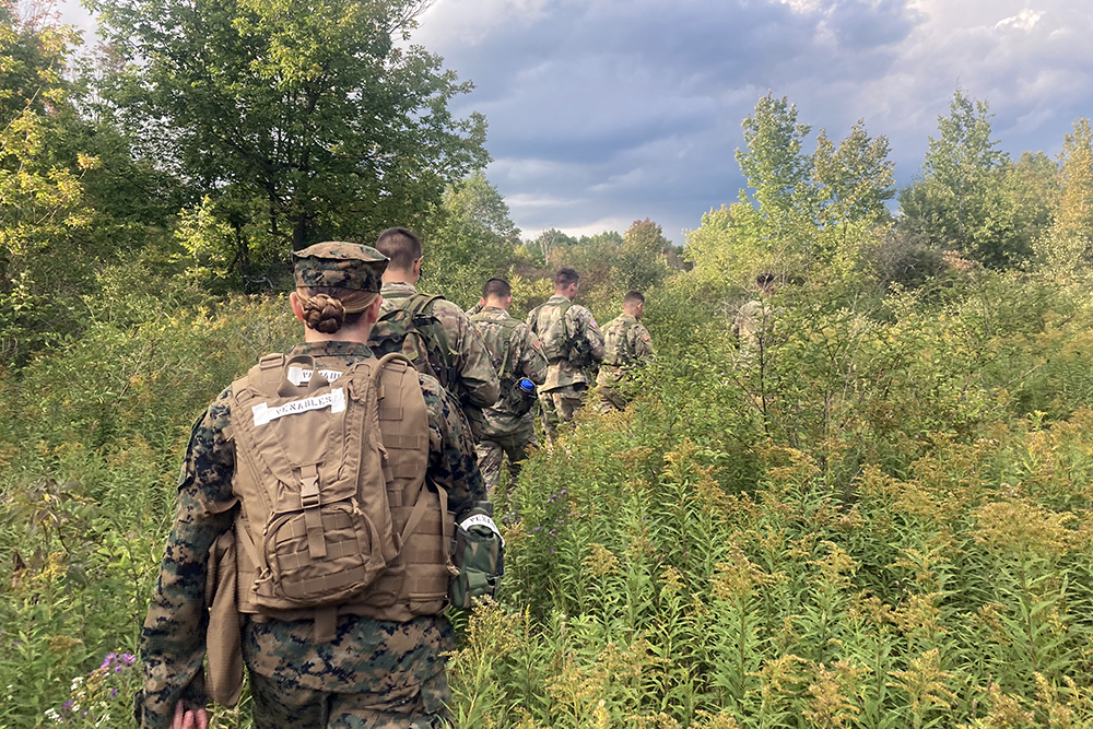 A group of midshipmen seen from behind on a trek through the brush.